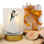 Bomboniera mini lampada in vetro decorato con raffigurazione di una coppia di sposi che ballano, perfetta come ricordo elegante e romantico. Funzionante a batteria, con confezione omaggio.